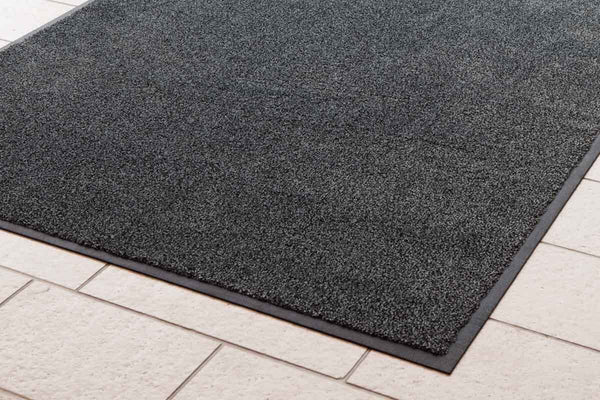 Anti Slip Floor Coating vs Mats: black rubber-backed non-slip floor mat on tiled surface for safety and traction.