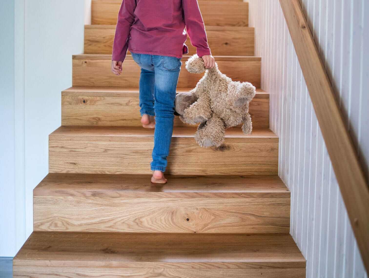 How to Make Stairs Non Slip & Safe for All - child carrying teddy bear up non-slip wooden stairs