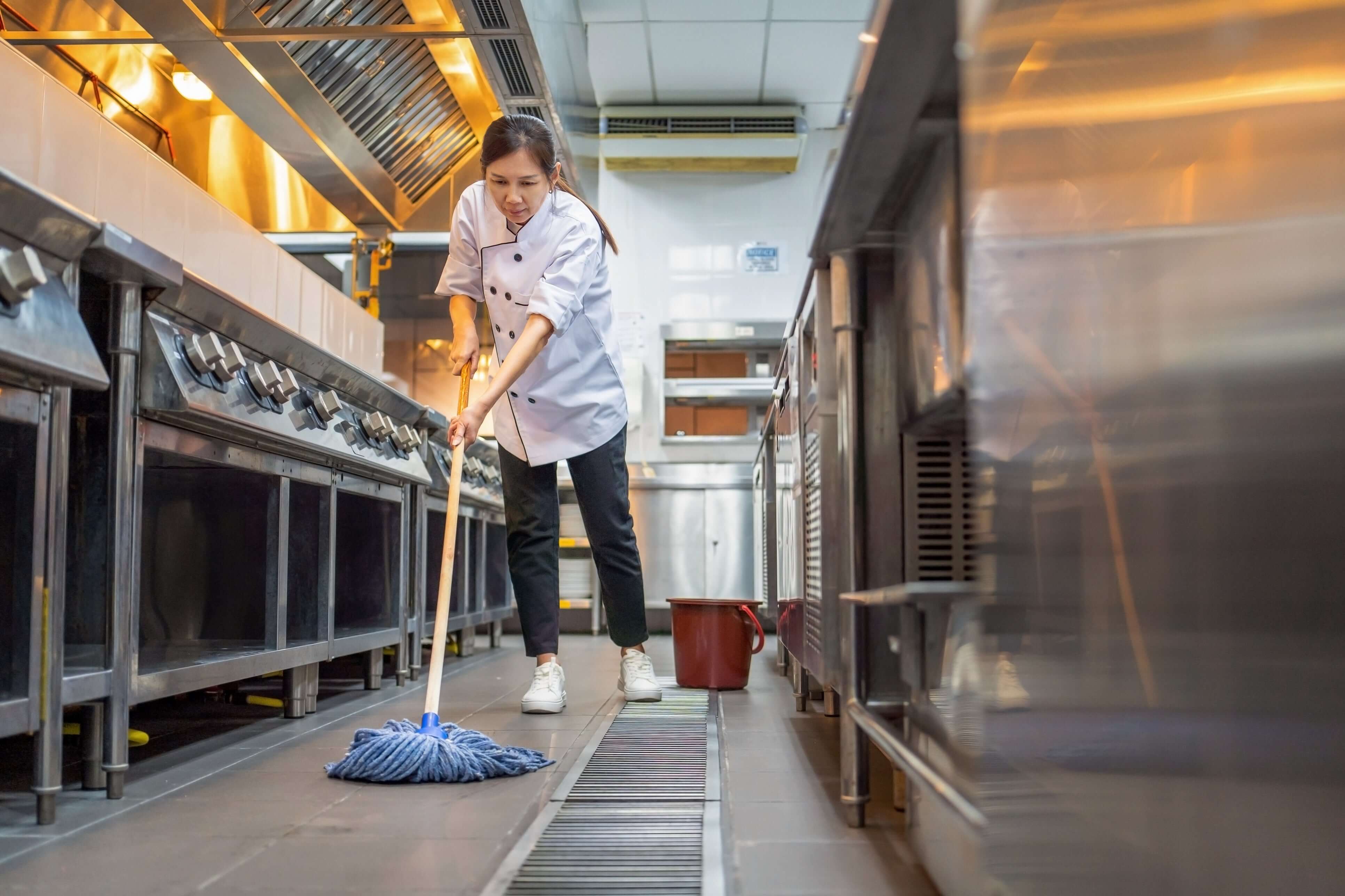 Commercial Kitchen Slip Testing: AS4586 P5 Requirements & Compliance Guide - kitchen staff mopping floor to prevent slips.