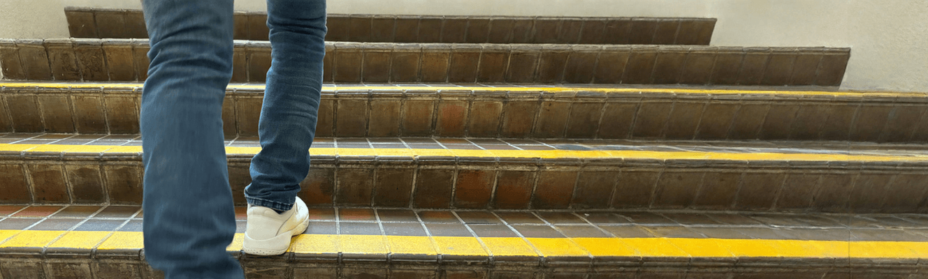 Person walking up tiled stairs featuring yellow stair nosing strips, demonstrating compliance with AS 1428.1 safety standards using Stellmann’s durable non-slip coating solution.